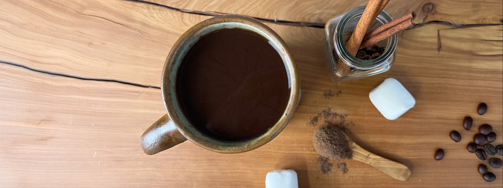 Mug of hot chocolate with marshmallows, cinnamon sticks, and coffee beans on a wooden surface