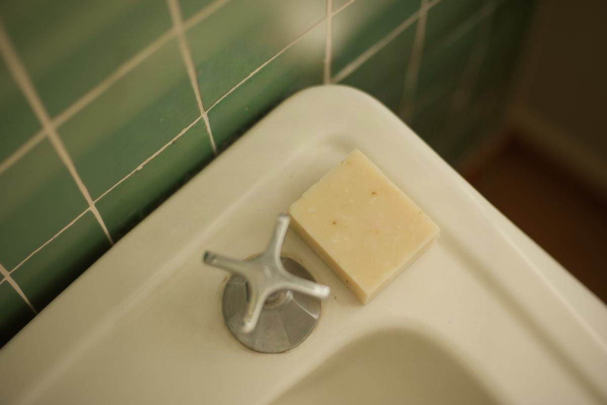 Bar of soap on a white sink with green tiled wall in the background