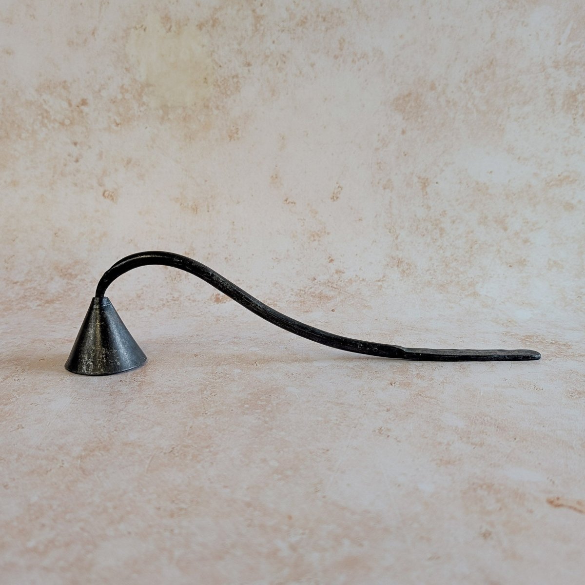 Black metal candle snuffer on a beige marble surface