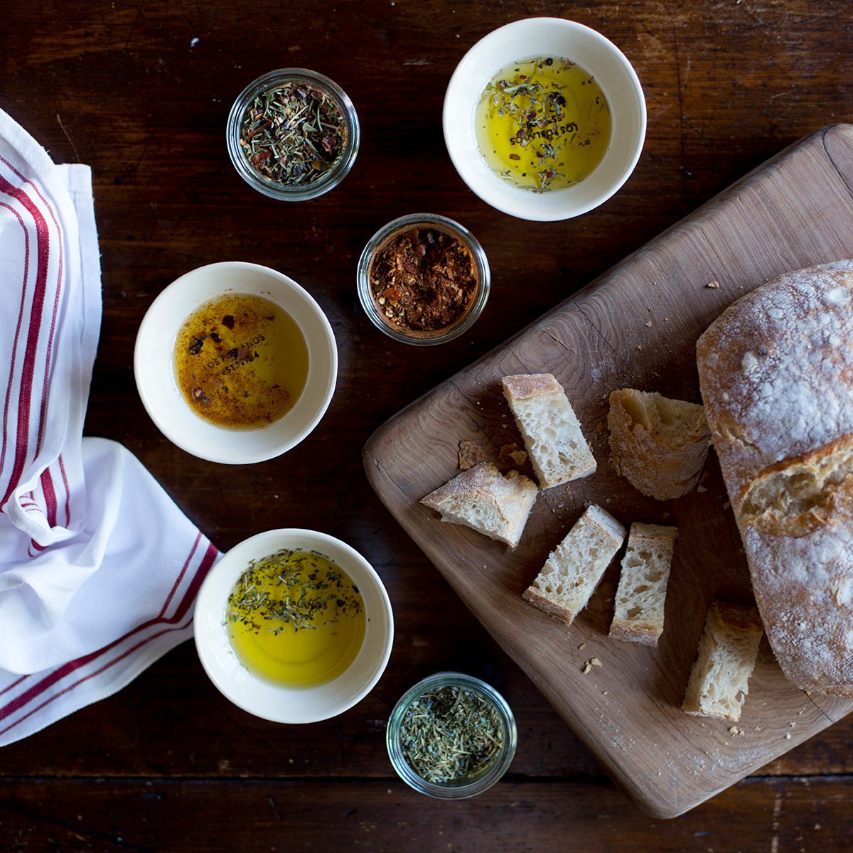 tiny bowls with olive oil, herbs and sliced bread on wooden table