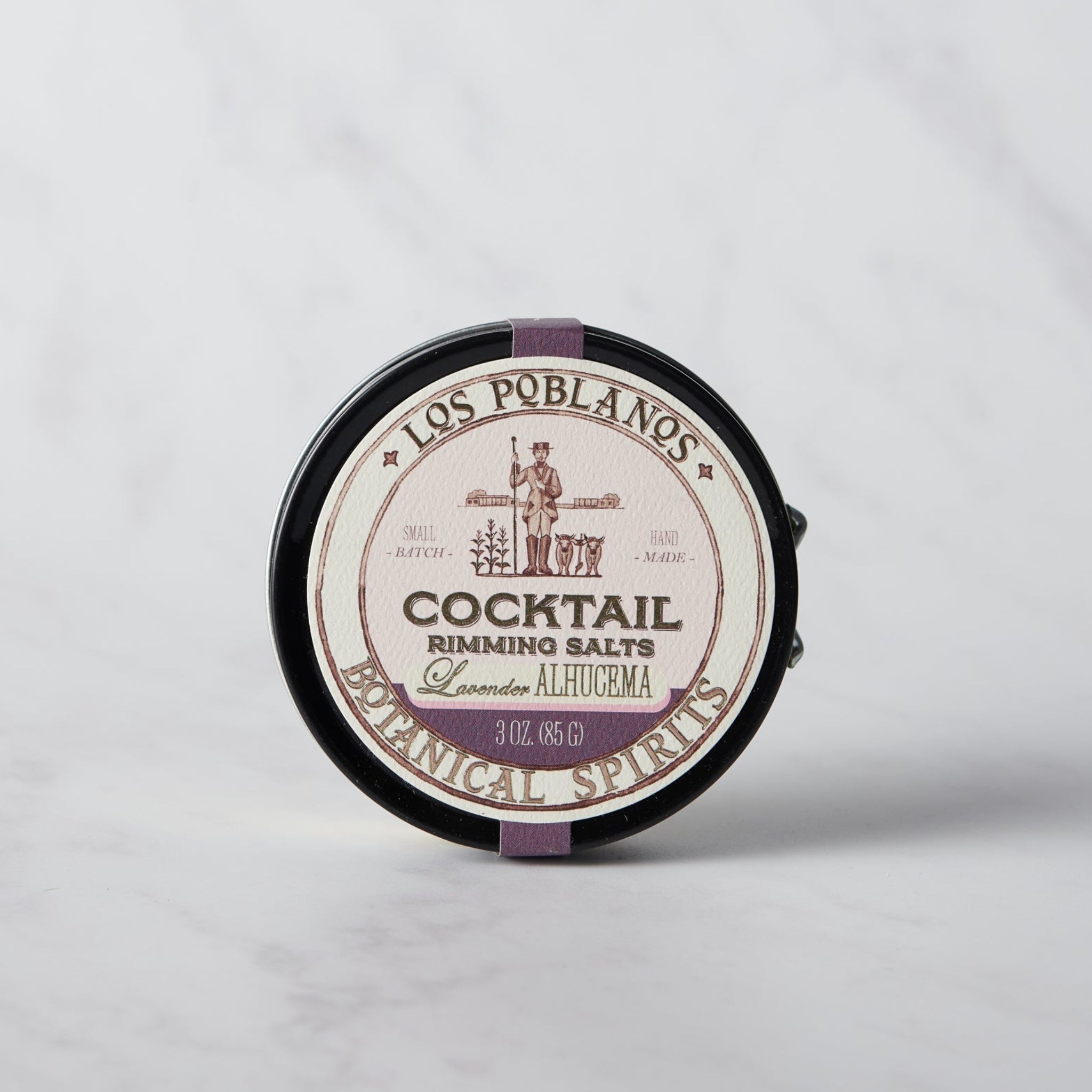 A round tin of Los Poblanos Cocktail Rimming Salt with lavender color visible through the transparent section on the lid.