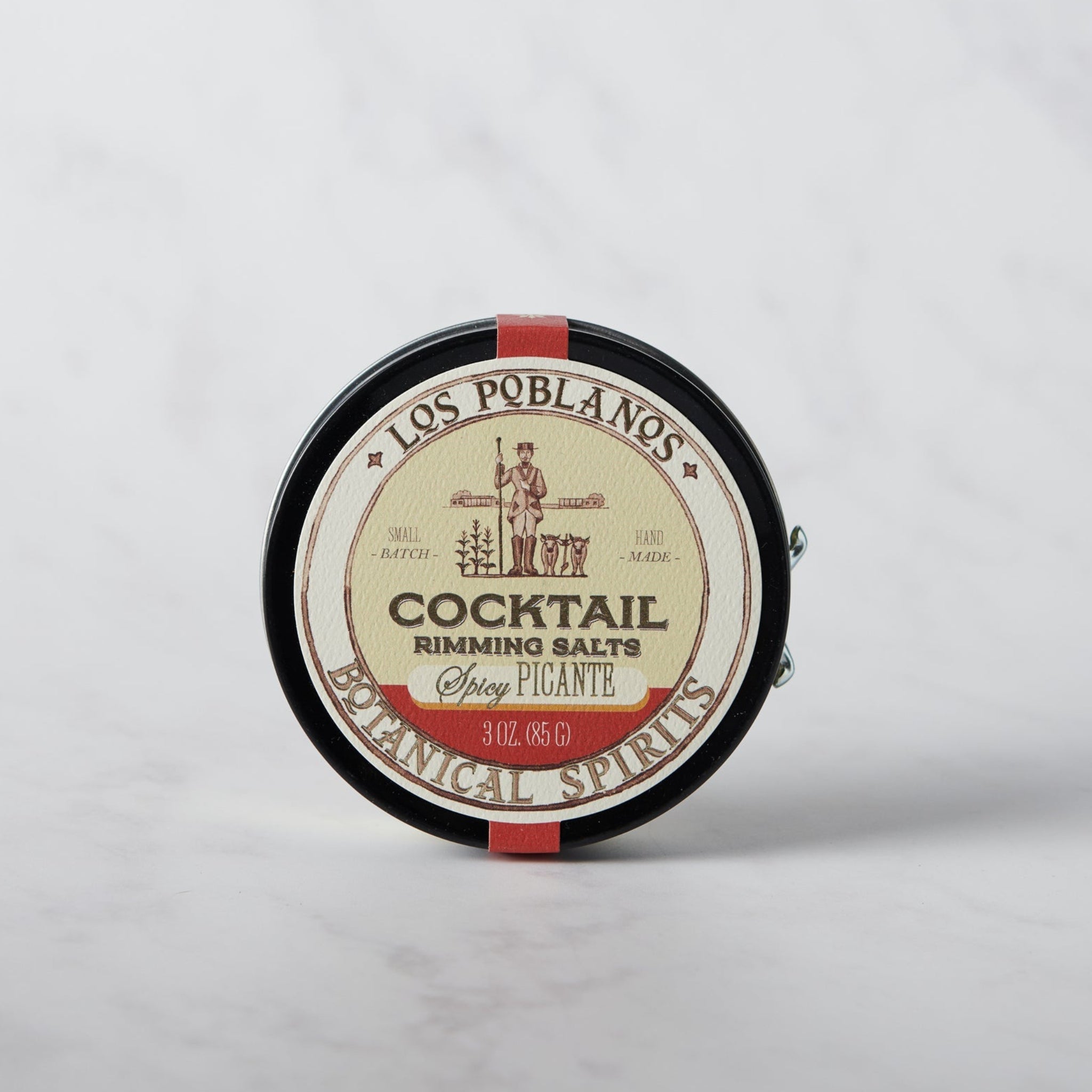 A round tin container of Los Poblanos Cocktail Rimming Salt - Spicy, with a label featuring an illustration of a pepper and text detailing the product.