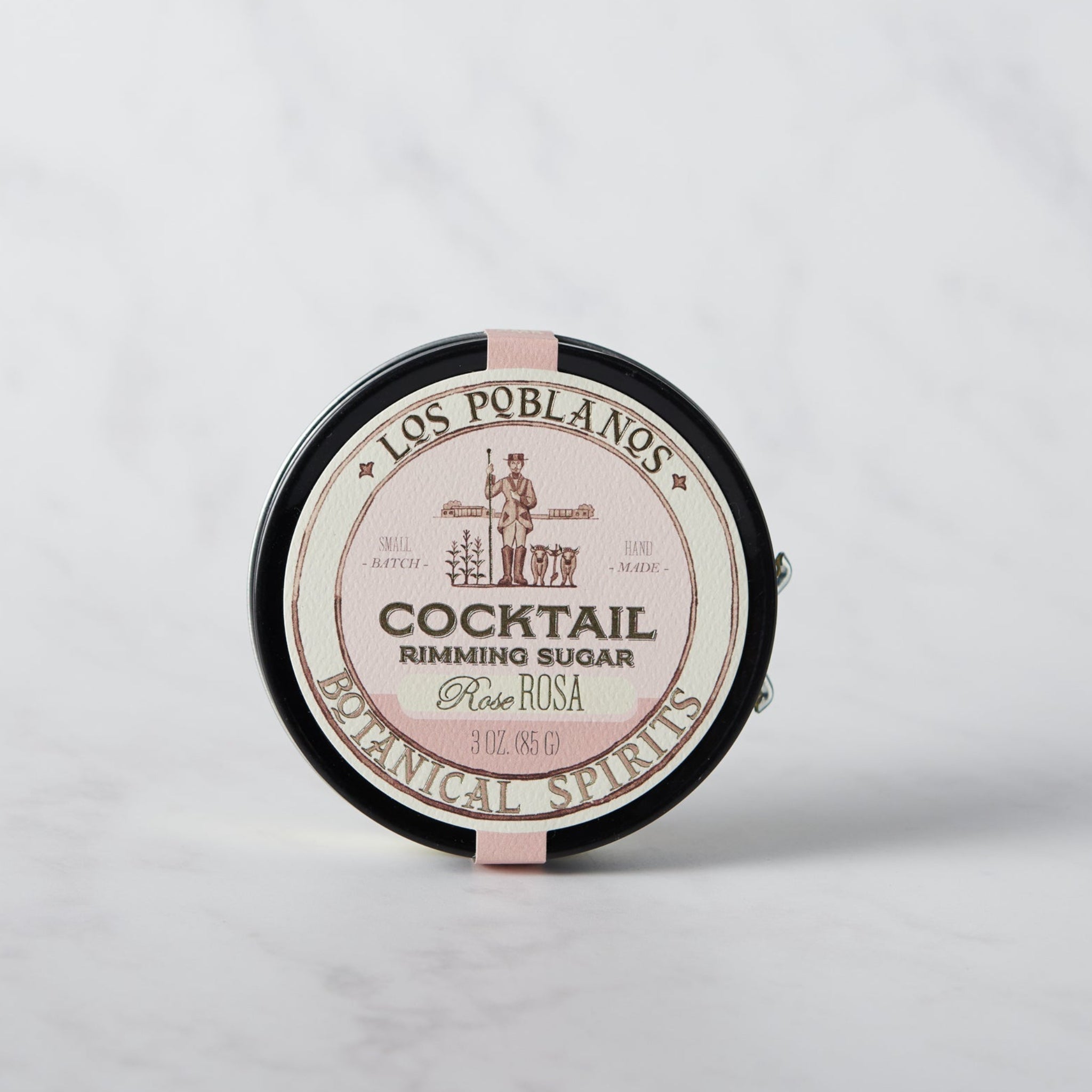 A round tin container of Los Poblanos Cocktail Rimming Sugar with rose flavor, placed on a marble surface.
