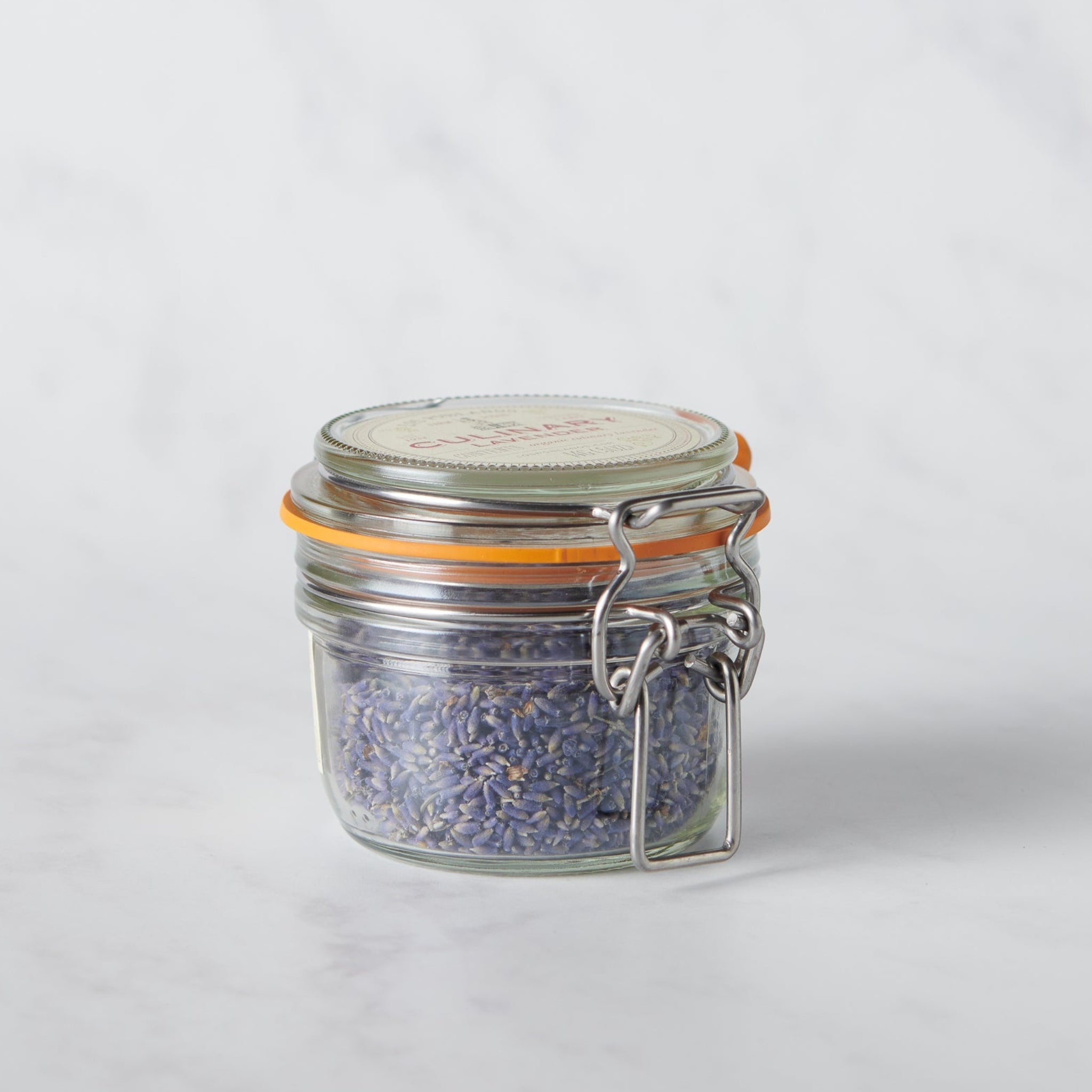 Small glass jar with metal lid containing a purple substance on a white background