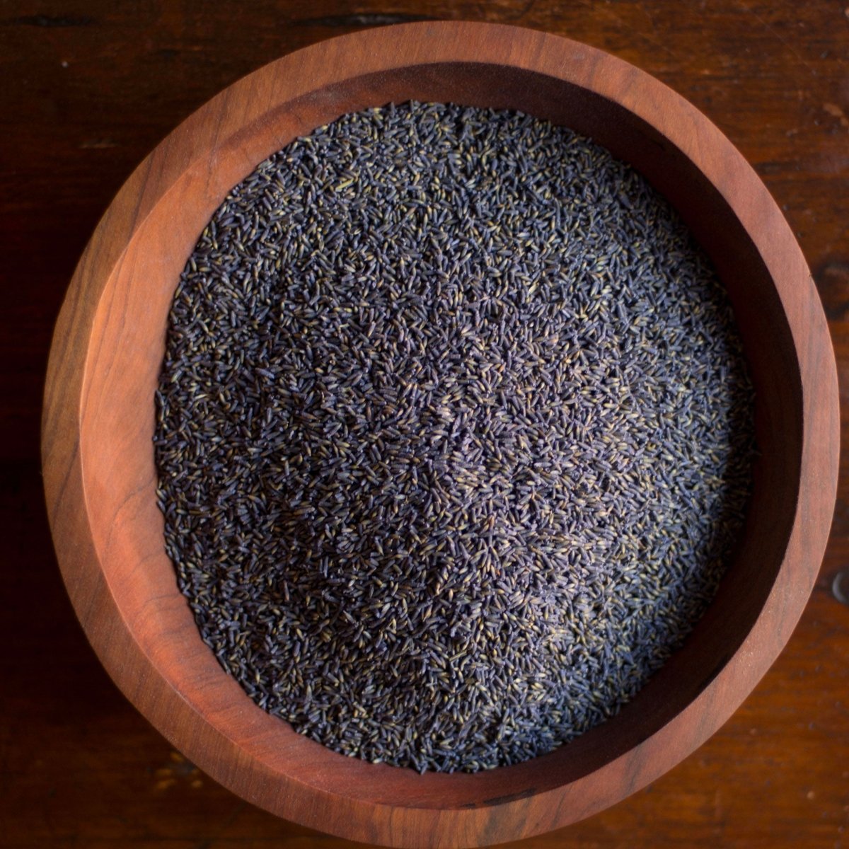 Wooden bowl filled with dried lavender flowers on a wooden surface