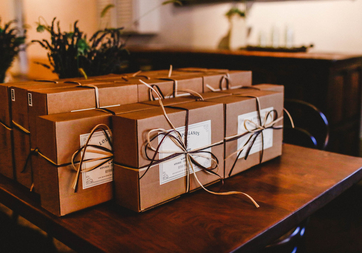 Several brown cardboard gift boxes tied with twine and labeled 'Longevity' are arranged on a wooden table in a warmly lit indoor setting.