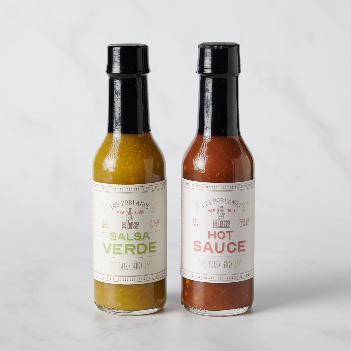 Two bottles of Los Poblanos hot sauce on a white marble background