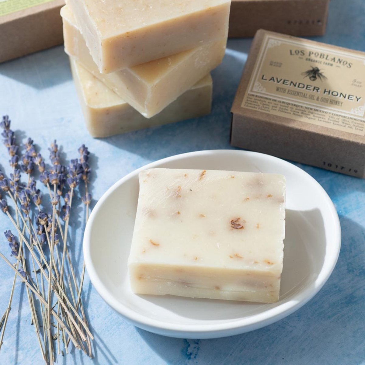 Bar of soap on a white plate with lavender and packaging in the background | Lavender Honey Bar Soap | Los Poblanos Farm Shop