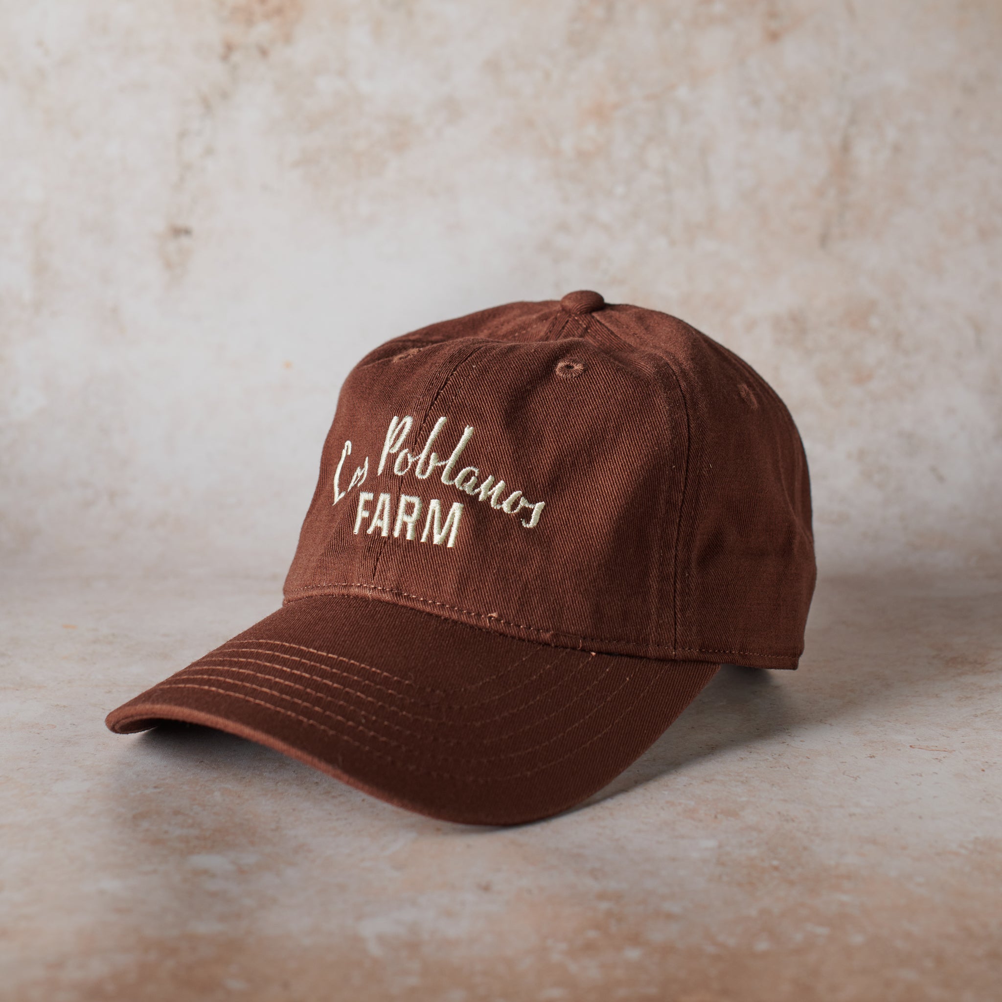 Brown cap with 'La Poblanos Farm' text on a beige background