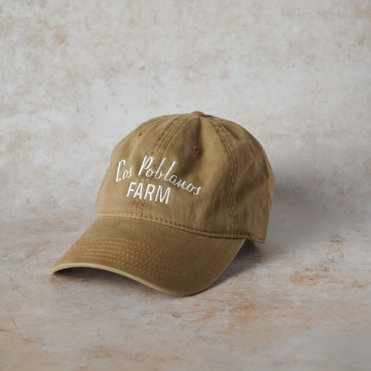 Brown cap with 'Los Poblanos Farm' text on a beige background