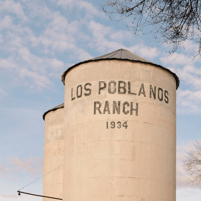 Silo with 'Los Poblanos Ranch 1934' text against a blue sky with clouds