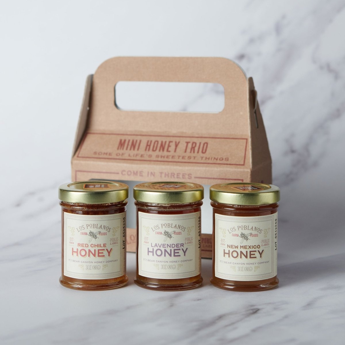 Mini honey trio with three jars and a cardboard carrier on a marble surface