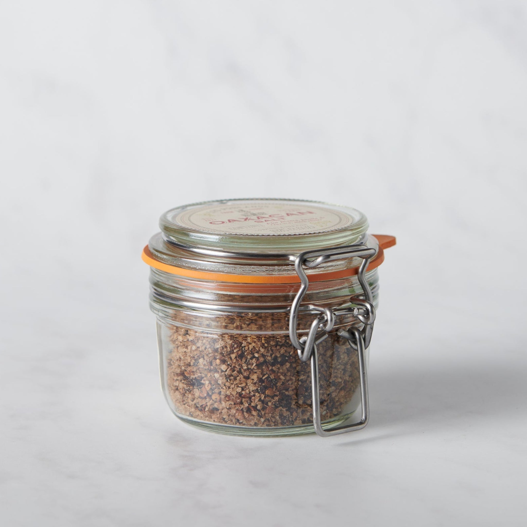Glass jar with a metal clasp full of chile mixed salt on a white background