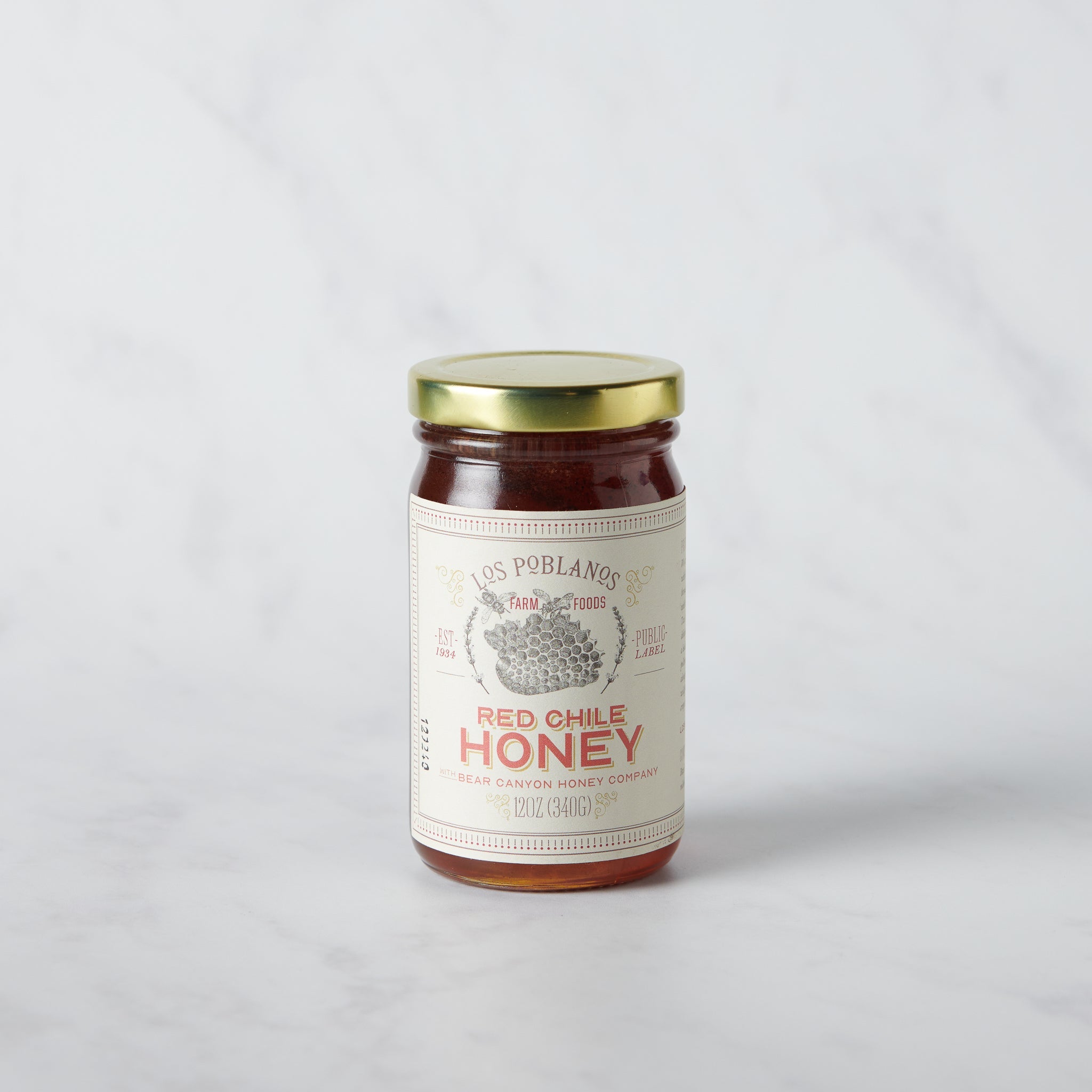 Jar of red chili honey with a gold lid on a light gray background