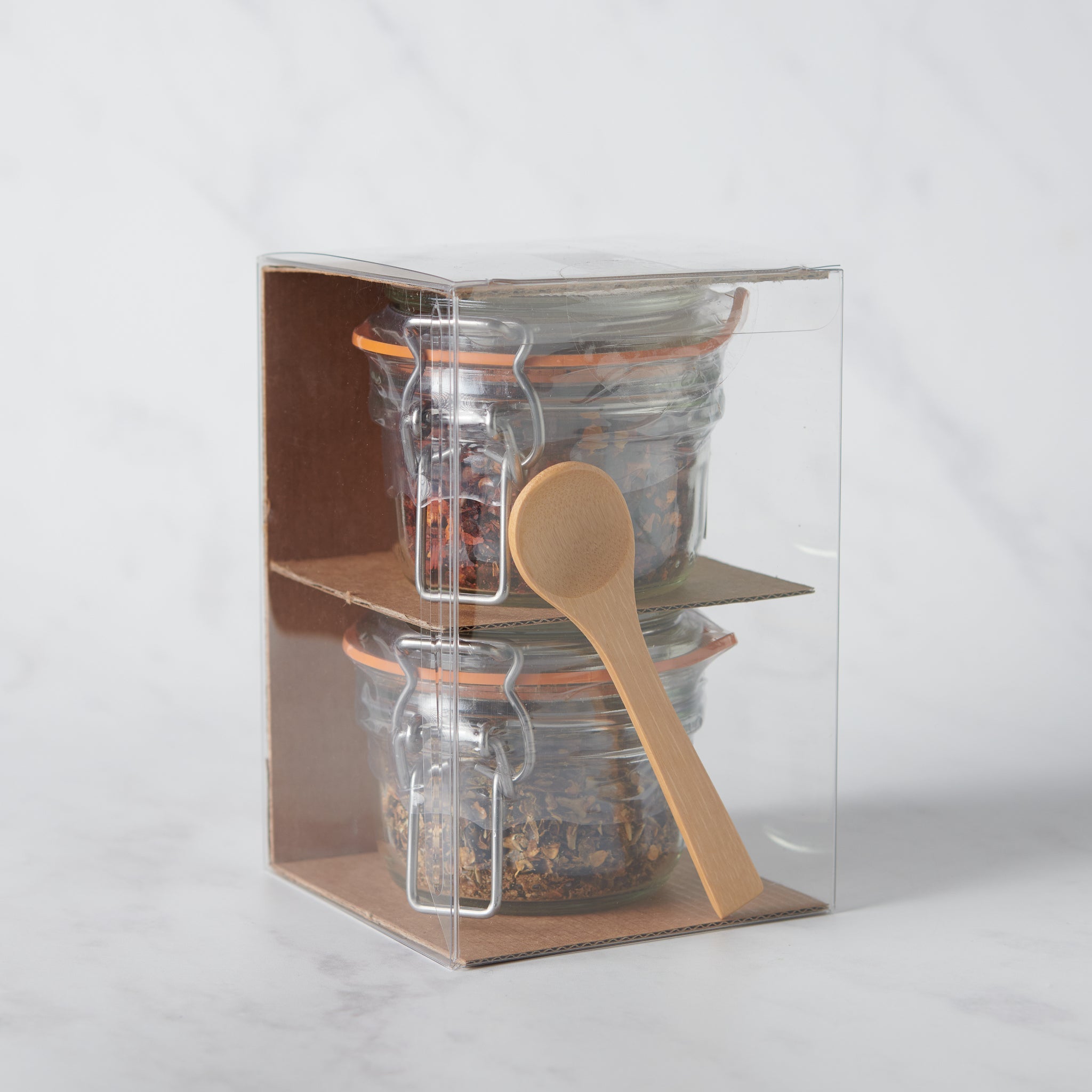 Clear packaging box with glass jars and a wooden spoon on a white background