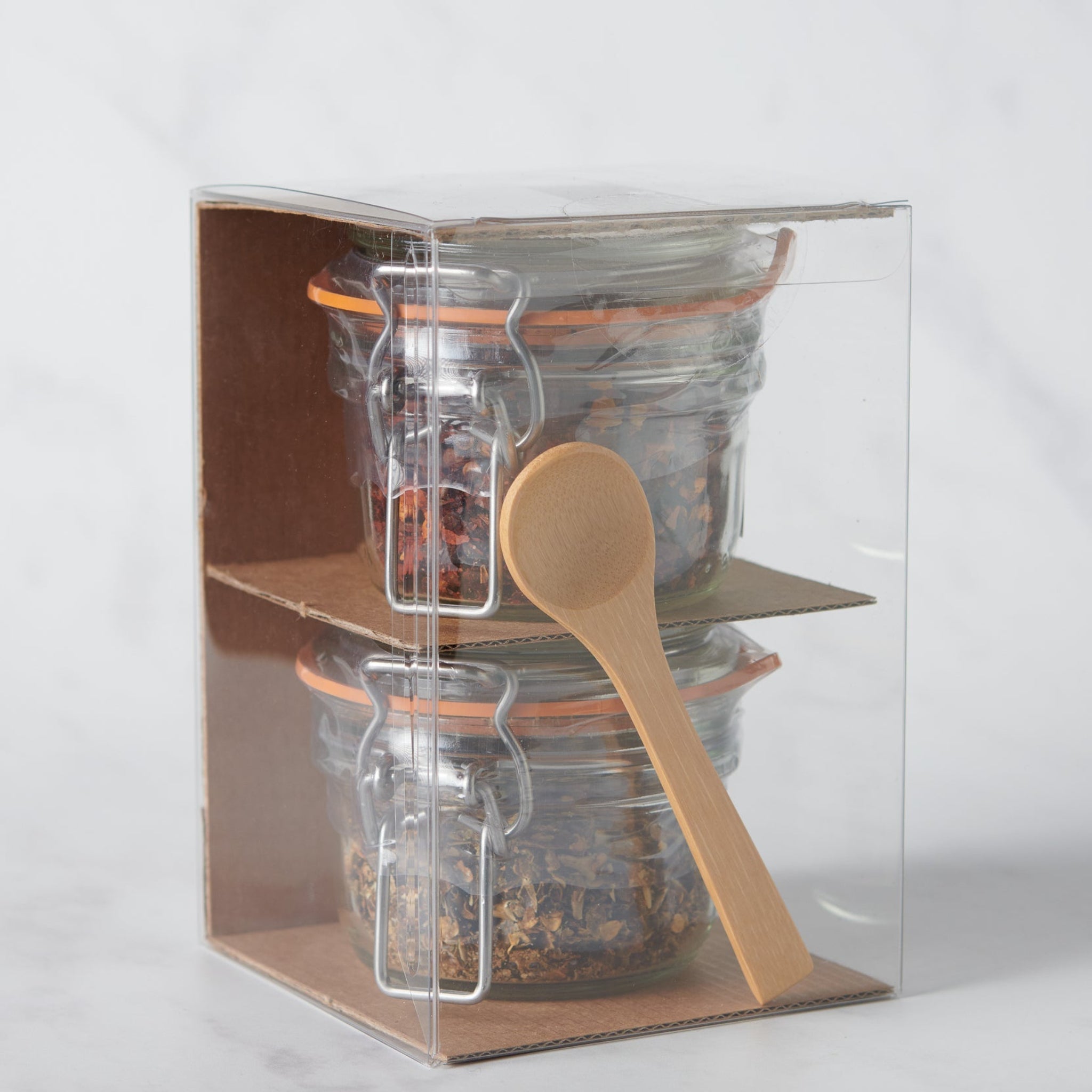 Clear packaging box with glass jars and a wooden spoon on a white background