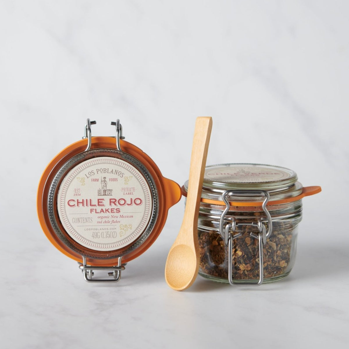 Jar of Chile Rojo flakes with a wooden spoon on a light gray background