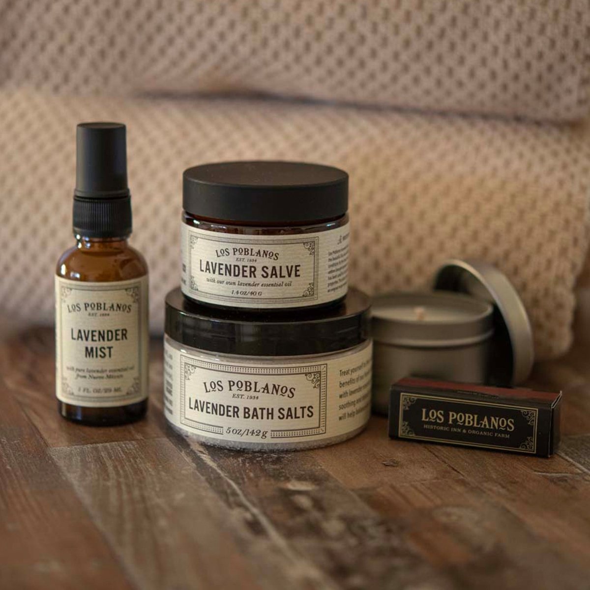 Collection of Los Poblanos skincare products including a bottle, jar, and bar on a wooden surface.