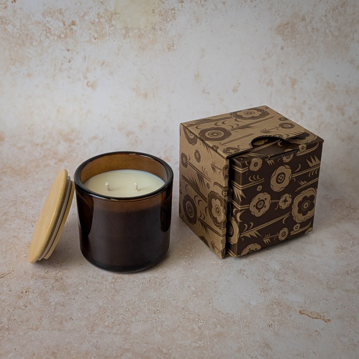 Candle in a brown jar with a decorative box on a textured surface