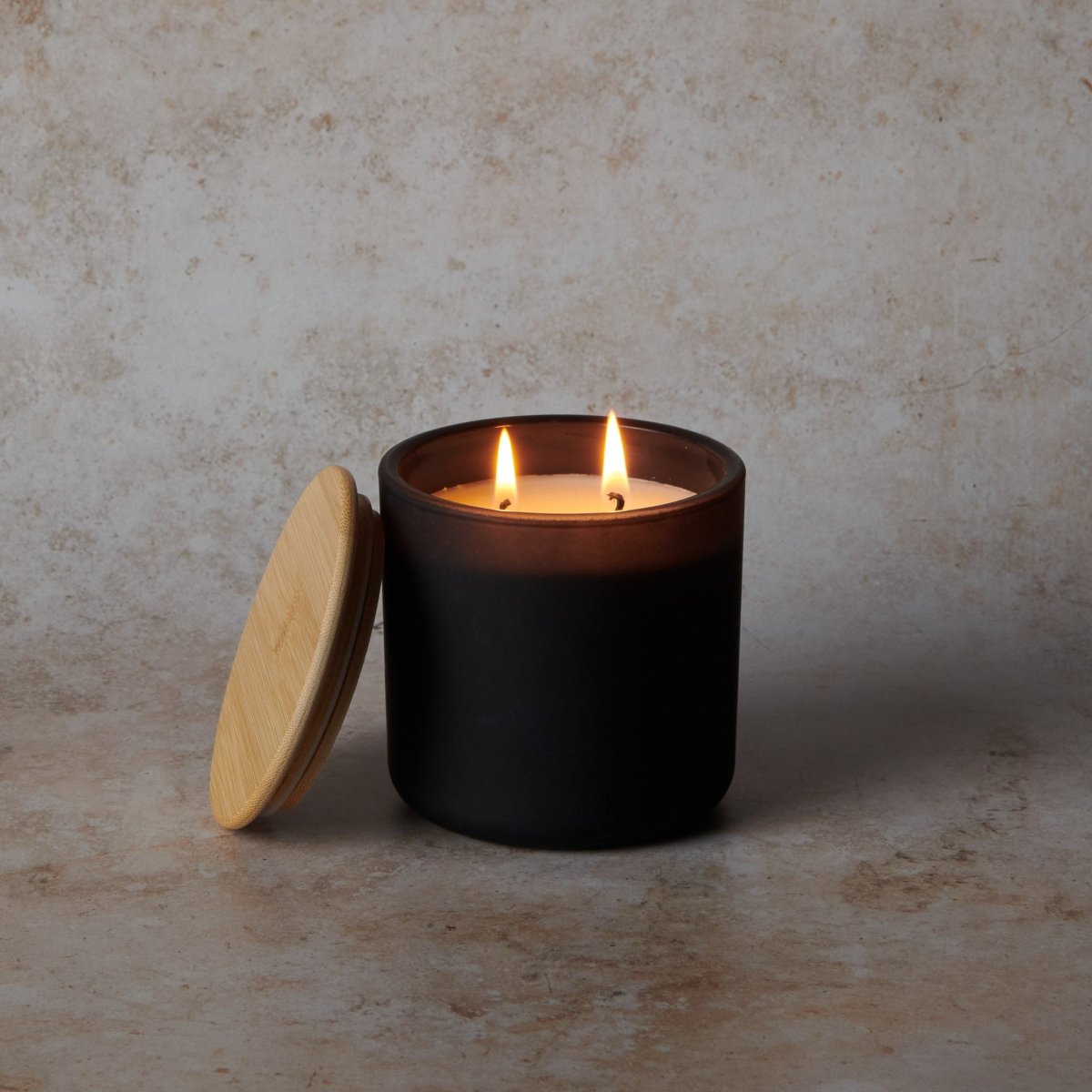 Black candle in a jar with a wooden lid on a textured beige surface