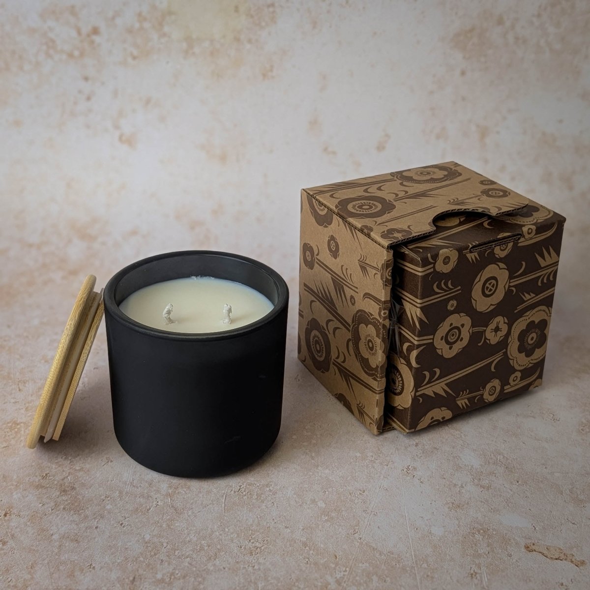 Black candle in a container with a decorative box on a textured surface