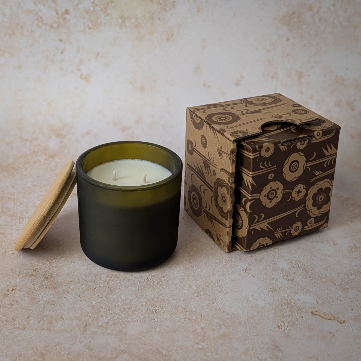 Black candle with a white wick next to a patterned cardboard box on a beige surface