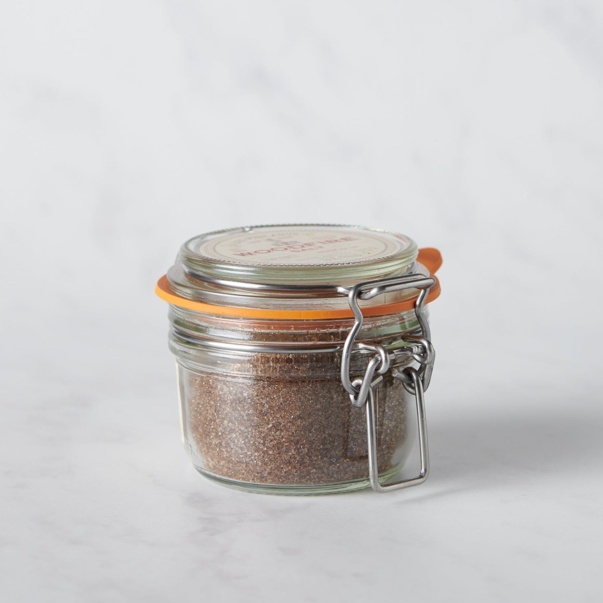 Glass jar with metal clasp full of smoked salt on a white background