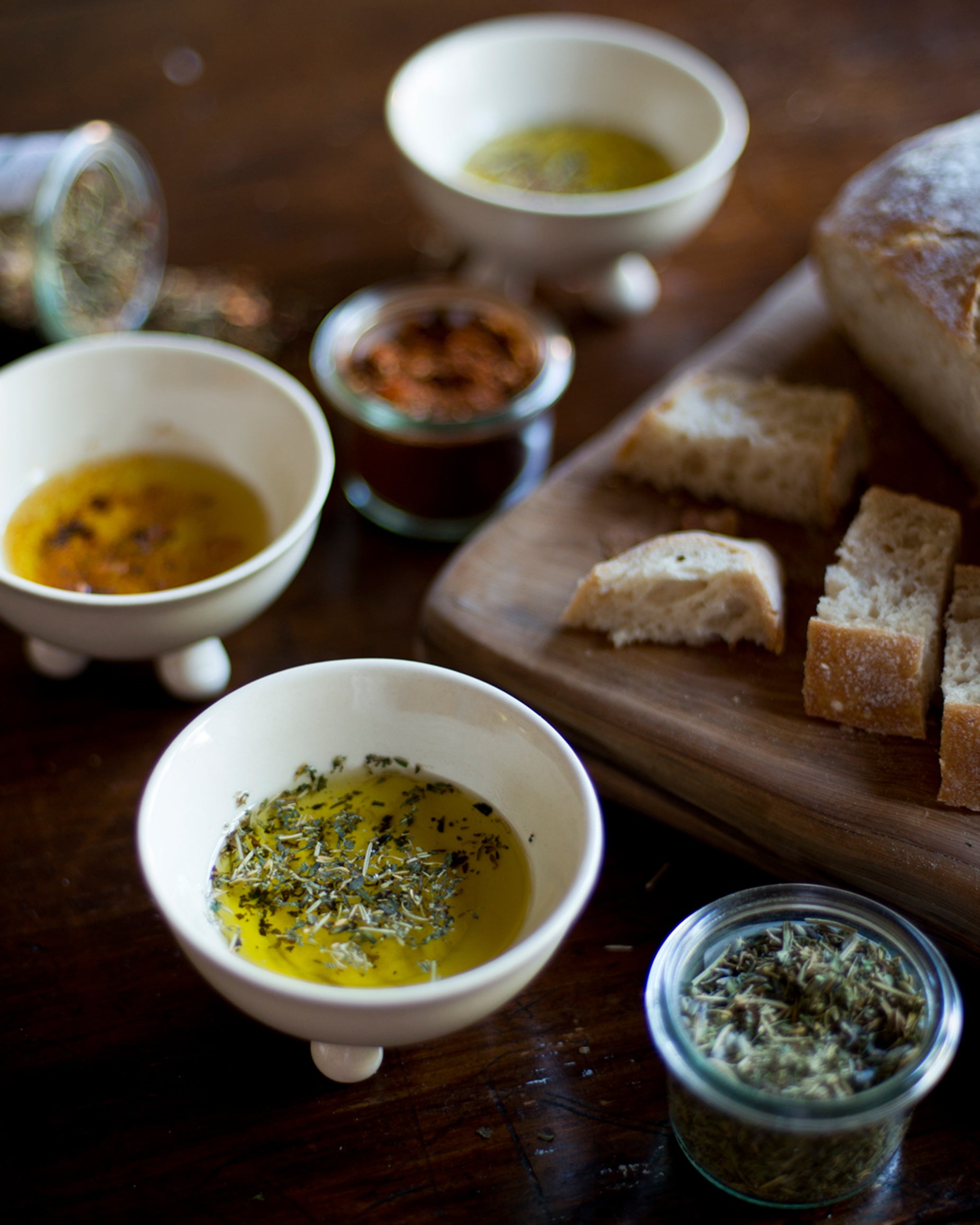 Assorted herbs in small bowls with bread slices on a wooden board