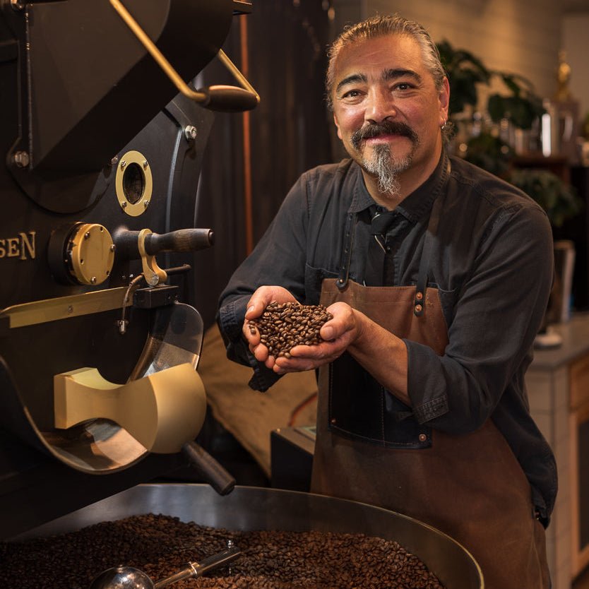 Man holding coffee beans next to a coffee roasting machine