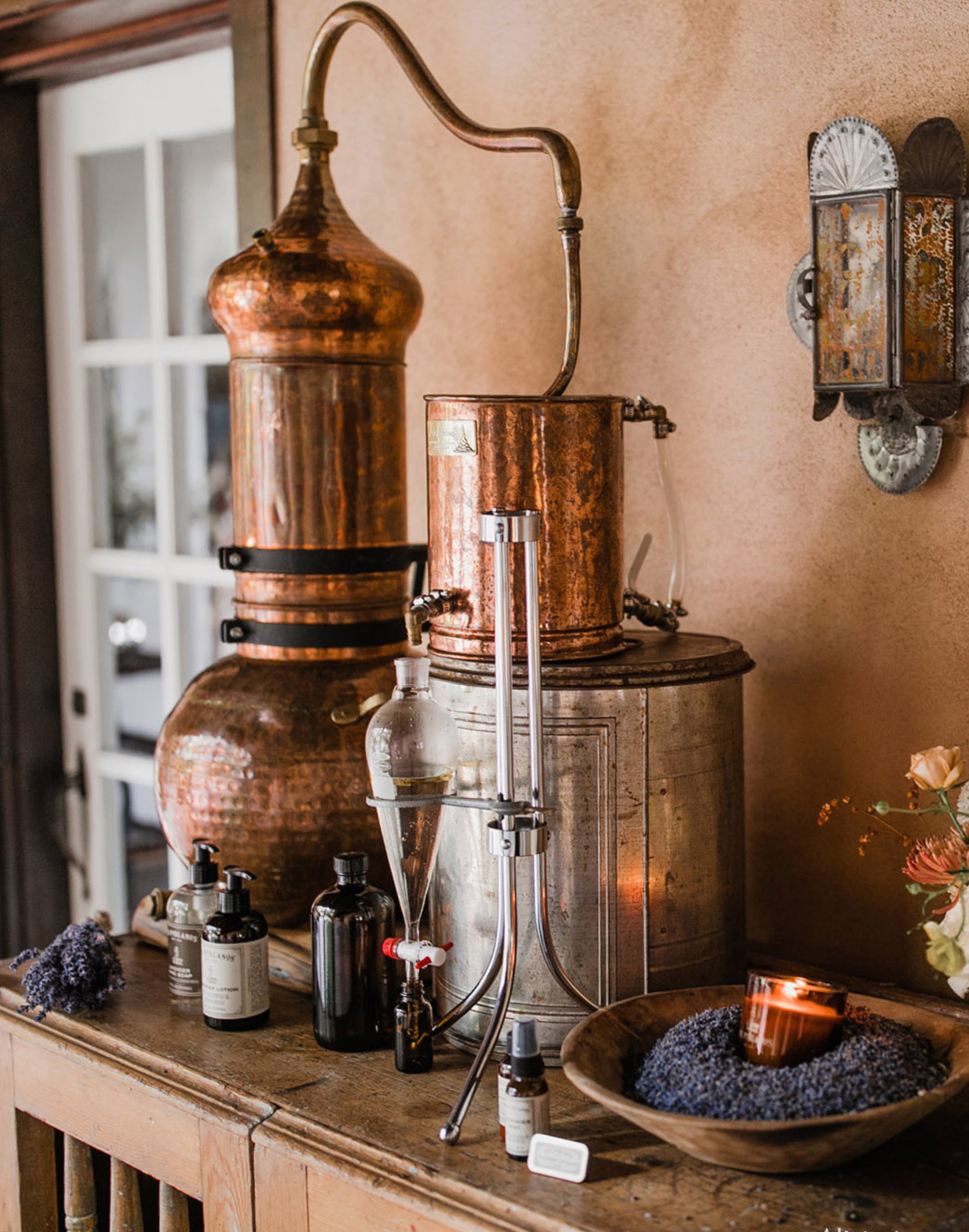 Copper still and alchemy bottles on a wooden table with a warm, rustic background.