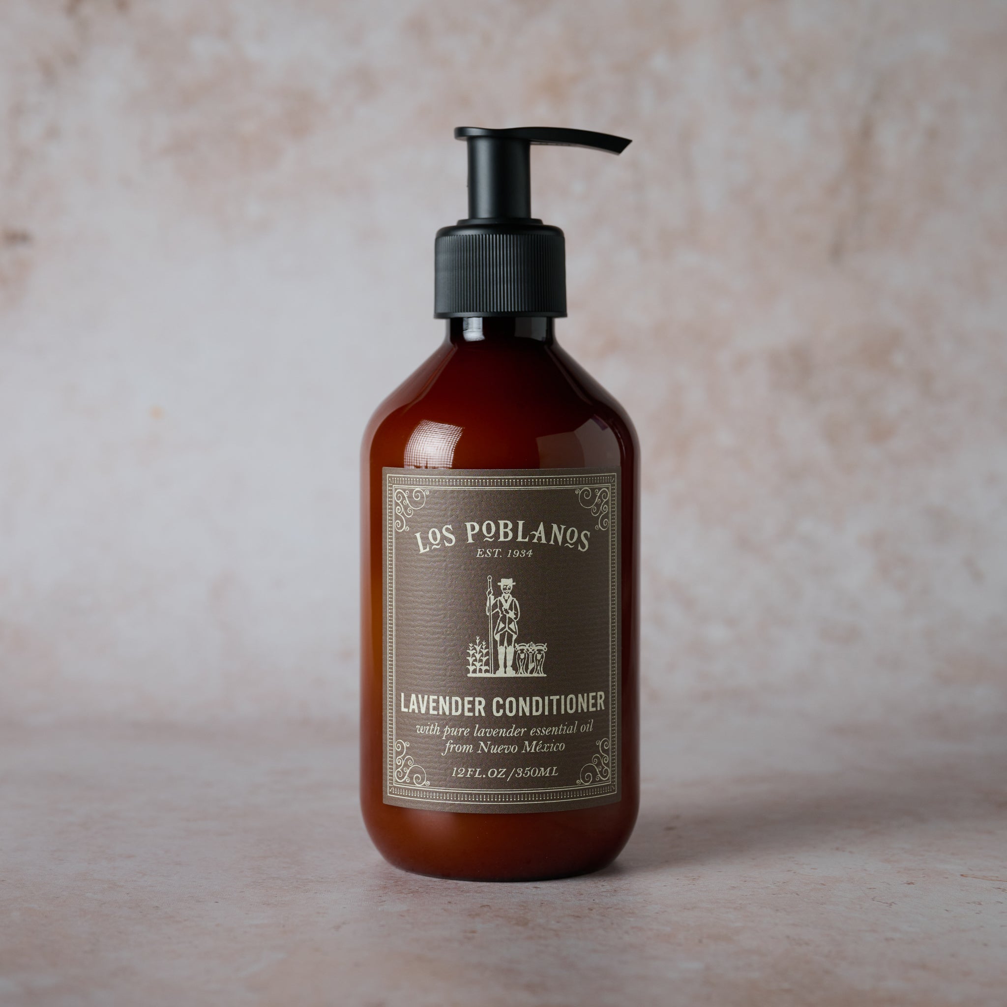 A brown bottle with a pump dispenser labeled 'Los Poblanos Lavender Conditioner', set against a textured beige background.