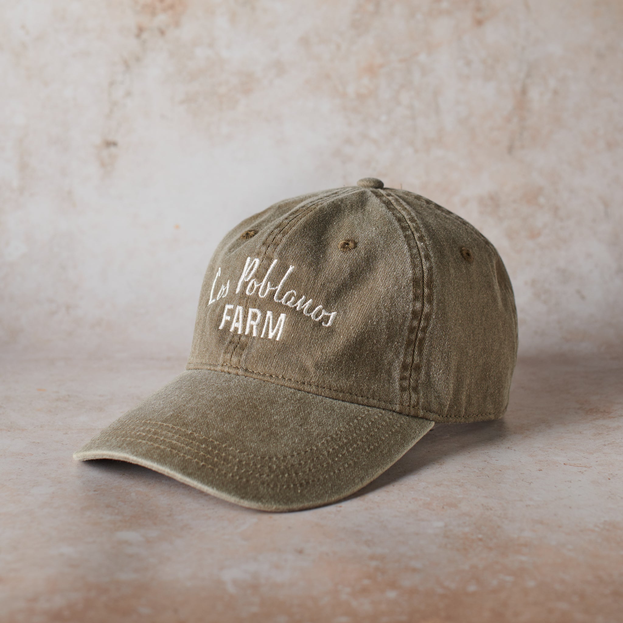 Olive green cap with 'Los Poblanos Farm' text on a beige background