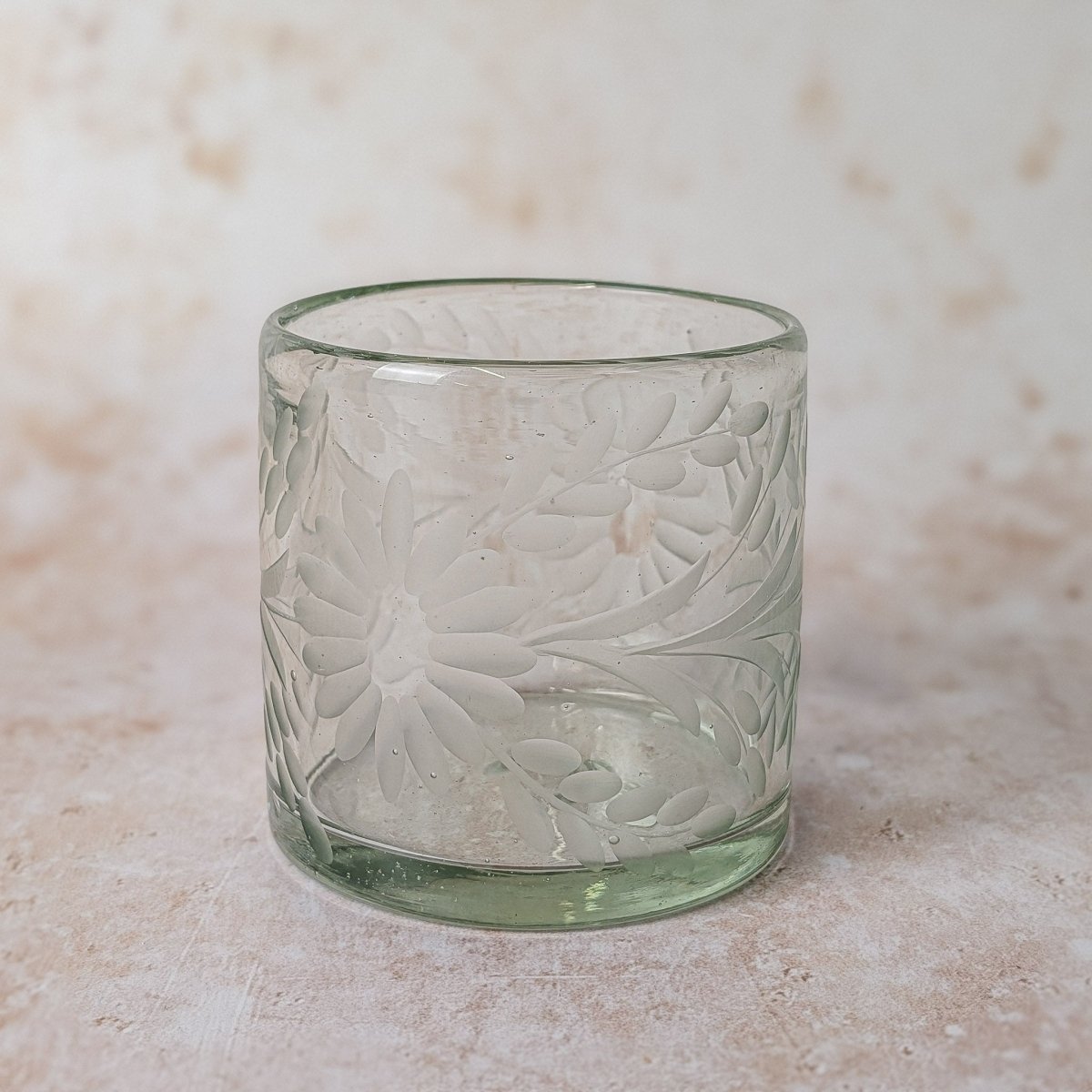 Green glass tumbler with floral patterns on a beige surface