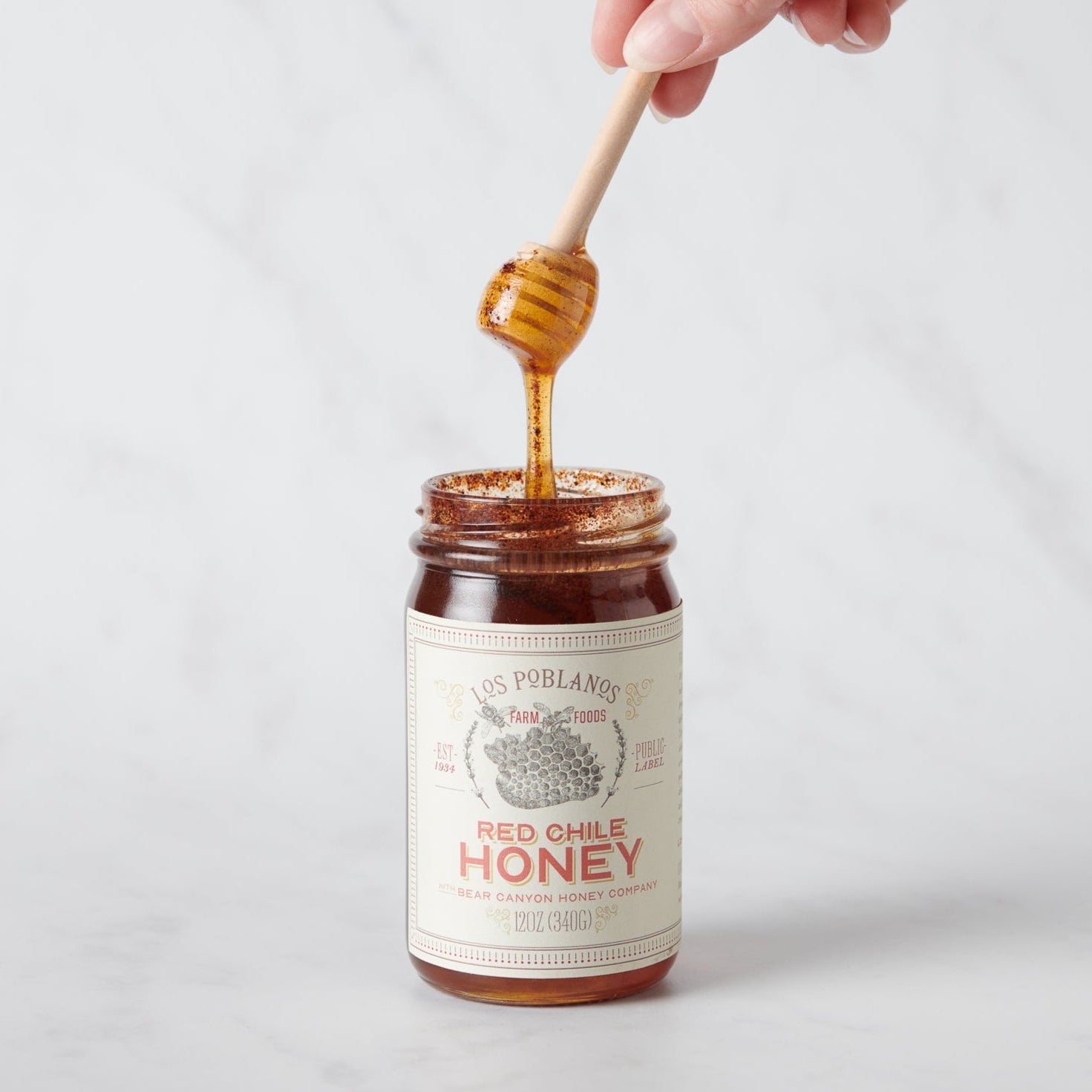 Jar of red chili honey with a honey dipper on a white background