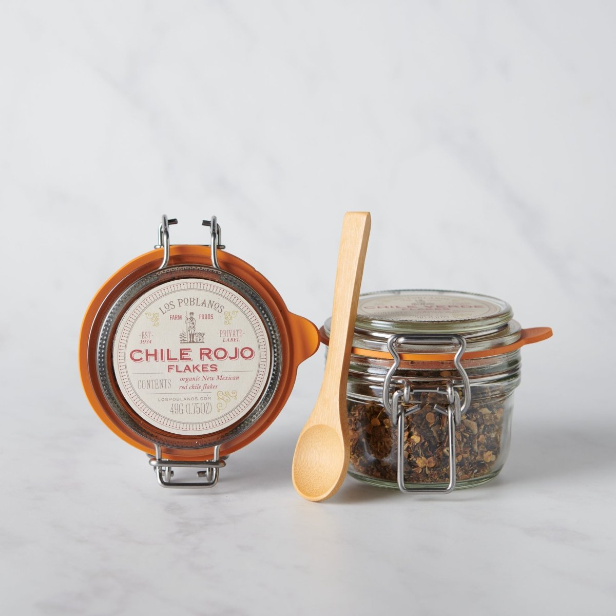 Jar of Chile Rojo flakes with a wooden spoon on a light gray background