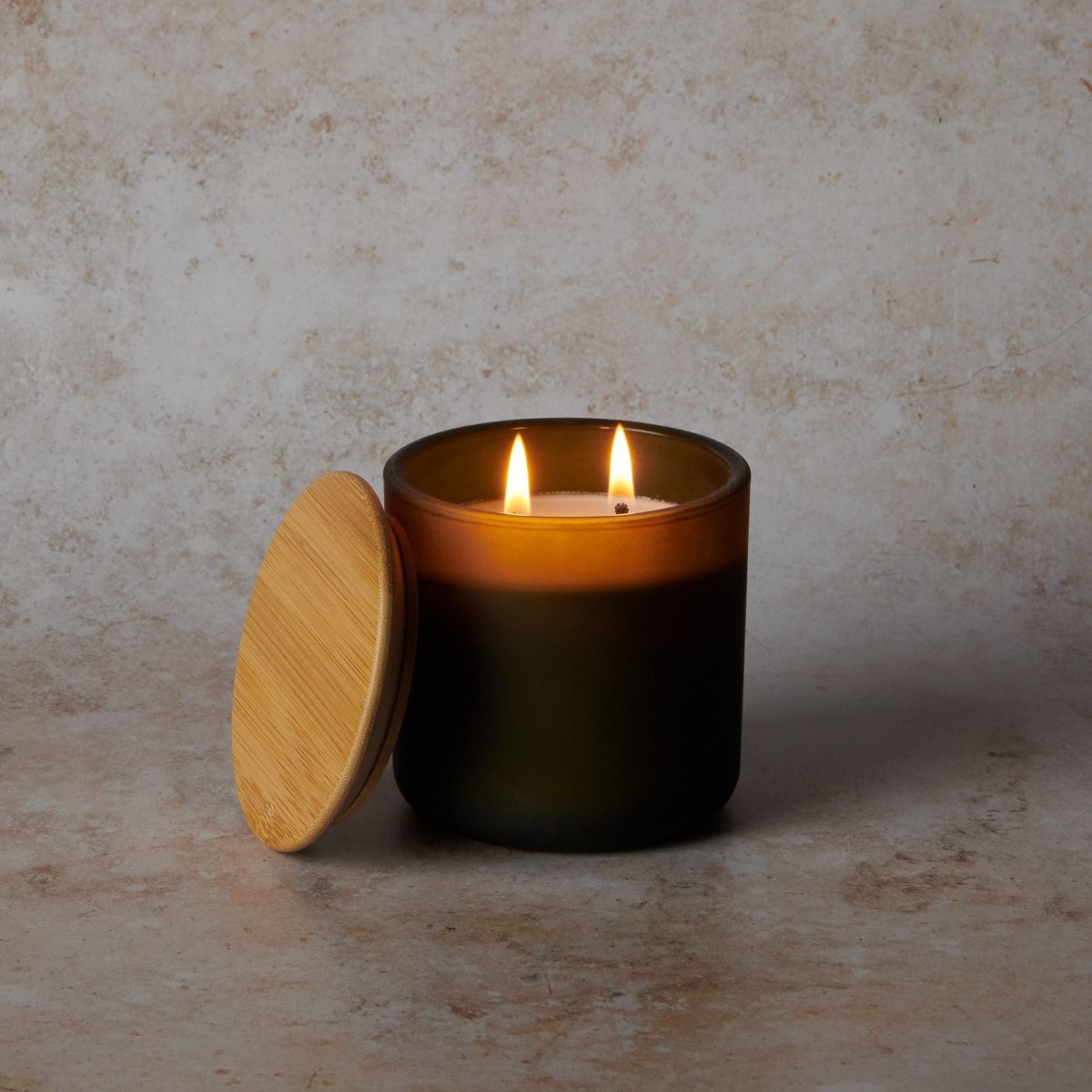 Candle in a glass container with a wooden lid on a textured surface