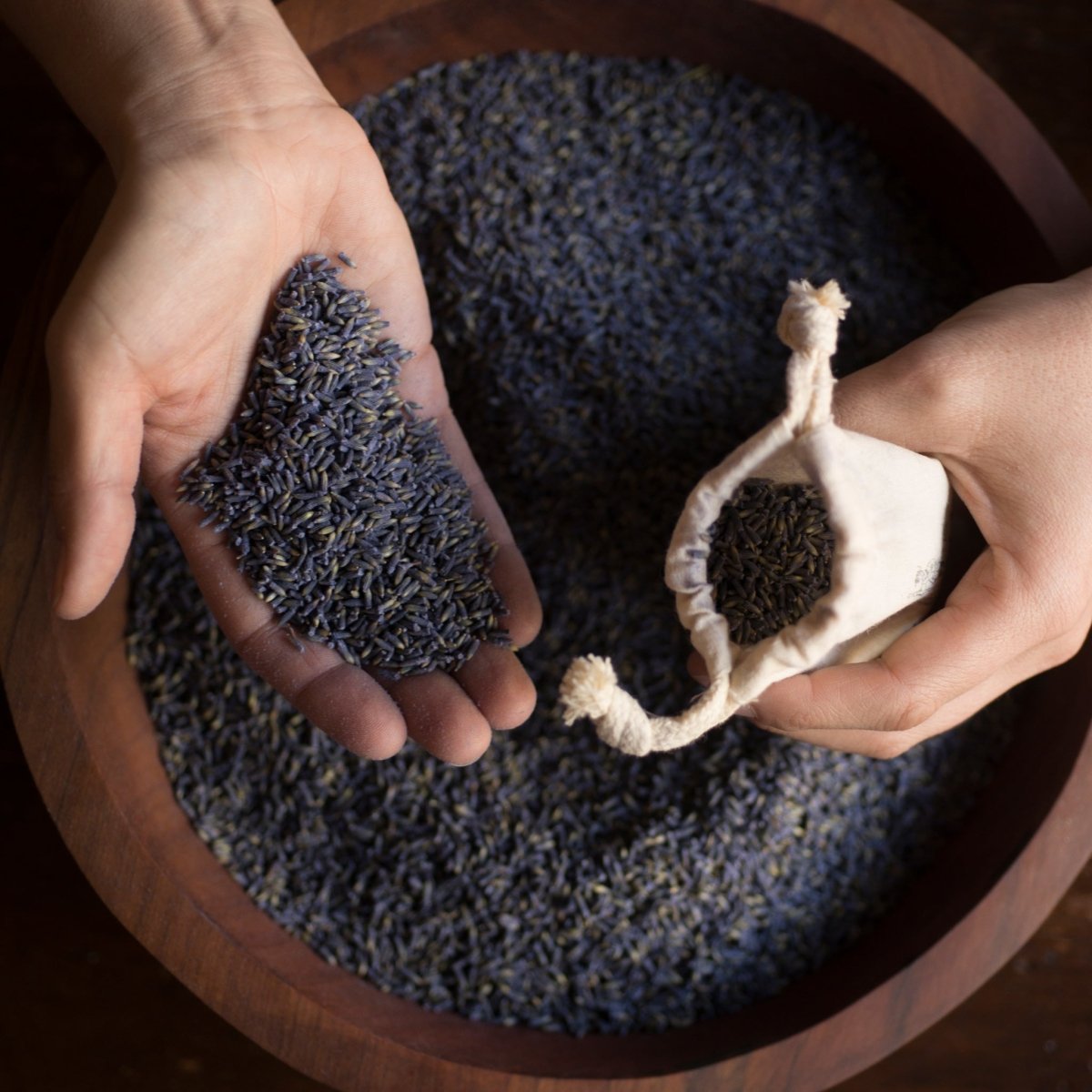 Hands holding dried lavender flowers above a wooden bowl filled with more lavender.