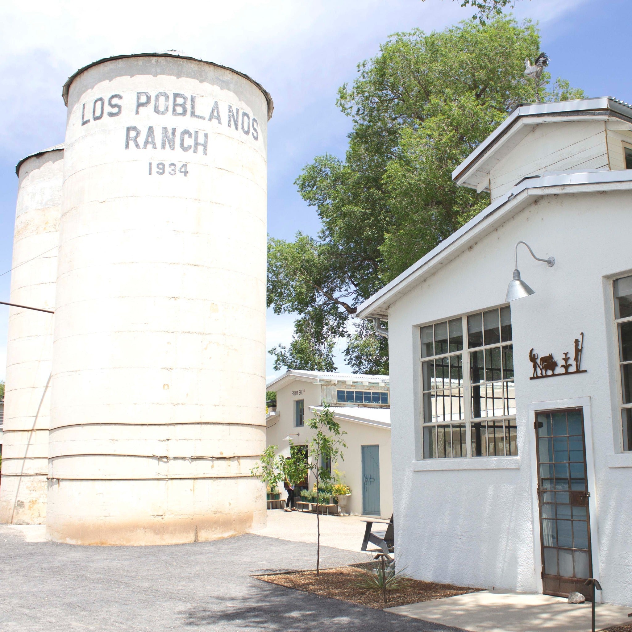 Silo with 'Los Poblanos Ranch 1934' text and a white building with decorative elements.